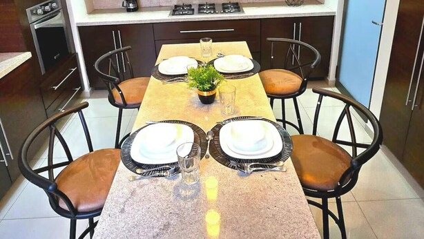 A modern kitchen with a central island, built-in appliances, and a dining area with chairs and a table set for four.