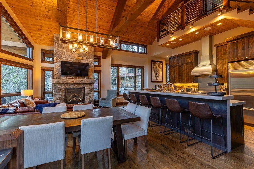 A spacious living area with a stone fireplace, wooden ceiling beams, and a large dining table with bar stools.