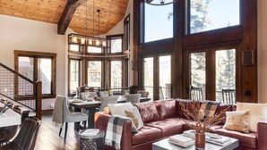 A spacious living area with a high ceiling, large windows, a leather sofa, and a dining table. - Apex - Walk to Trails + Hot Tub | Sauna & Theater (Mountain Village)