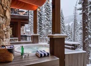 A wooden deck with a hot tub, a basket, and a bottle, surrounded by snow-covered trees and a mountain view. - Apex - Walk to Trails + Hot Tub | Sauna & Theater (Mountain Village)