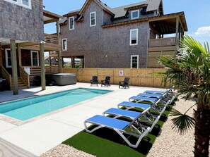 A swimming pool with lounge chairs, a hot tub, and a wooden deck area.