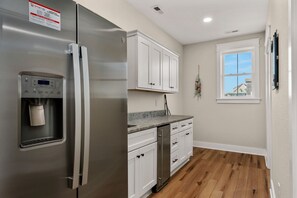 A kitchen with a stainless steel refrigerator, white cabinets, a water dispenser, and a window with a view.