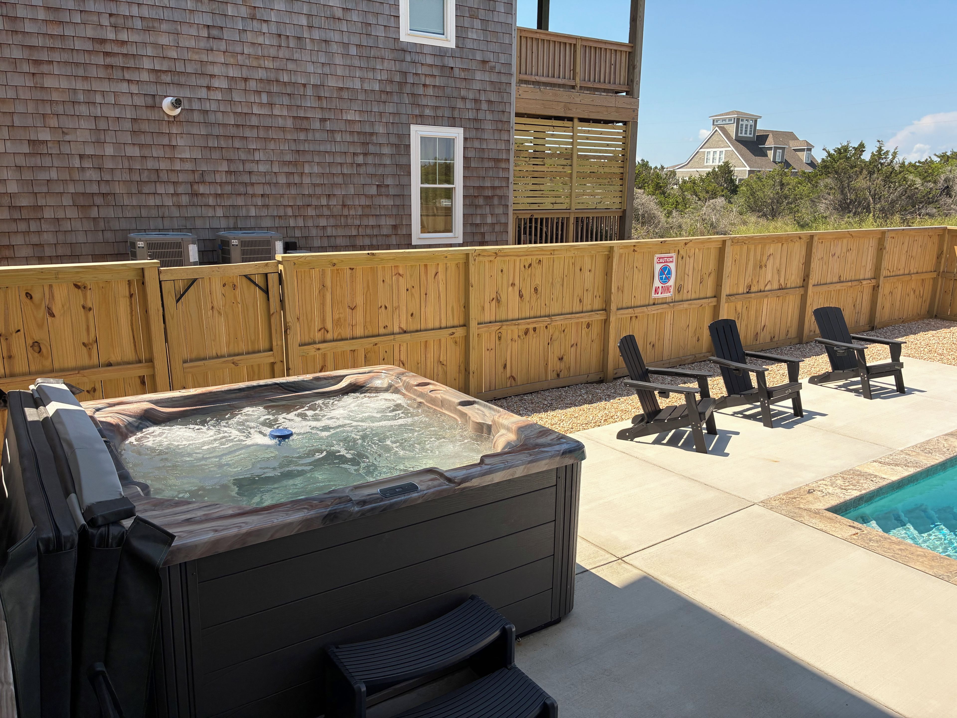 A backyard with a hot tub, outdoor seating, and a wooden fence.