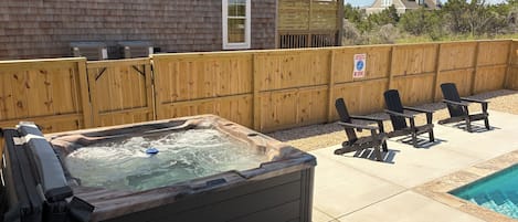 Un jardin avec un jacuzzi, un espace salon extérieur et une clôture en bois.