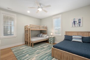 Une chambre avec un lit superposé, un lit simple, un ventilateur de plafond et un tableau au mur.