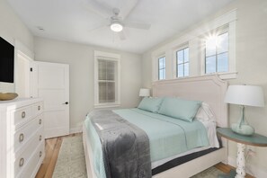 Une chambre à coucher comprenant un lit, une commode, une table de chevet, une lampe, une fenêtre et un ventilateur de plafond.