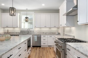A modern kitchen with white cabinets, a stainless steel stove, and a window with blinds.
