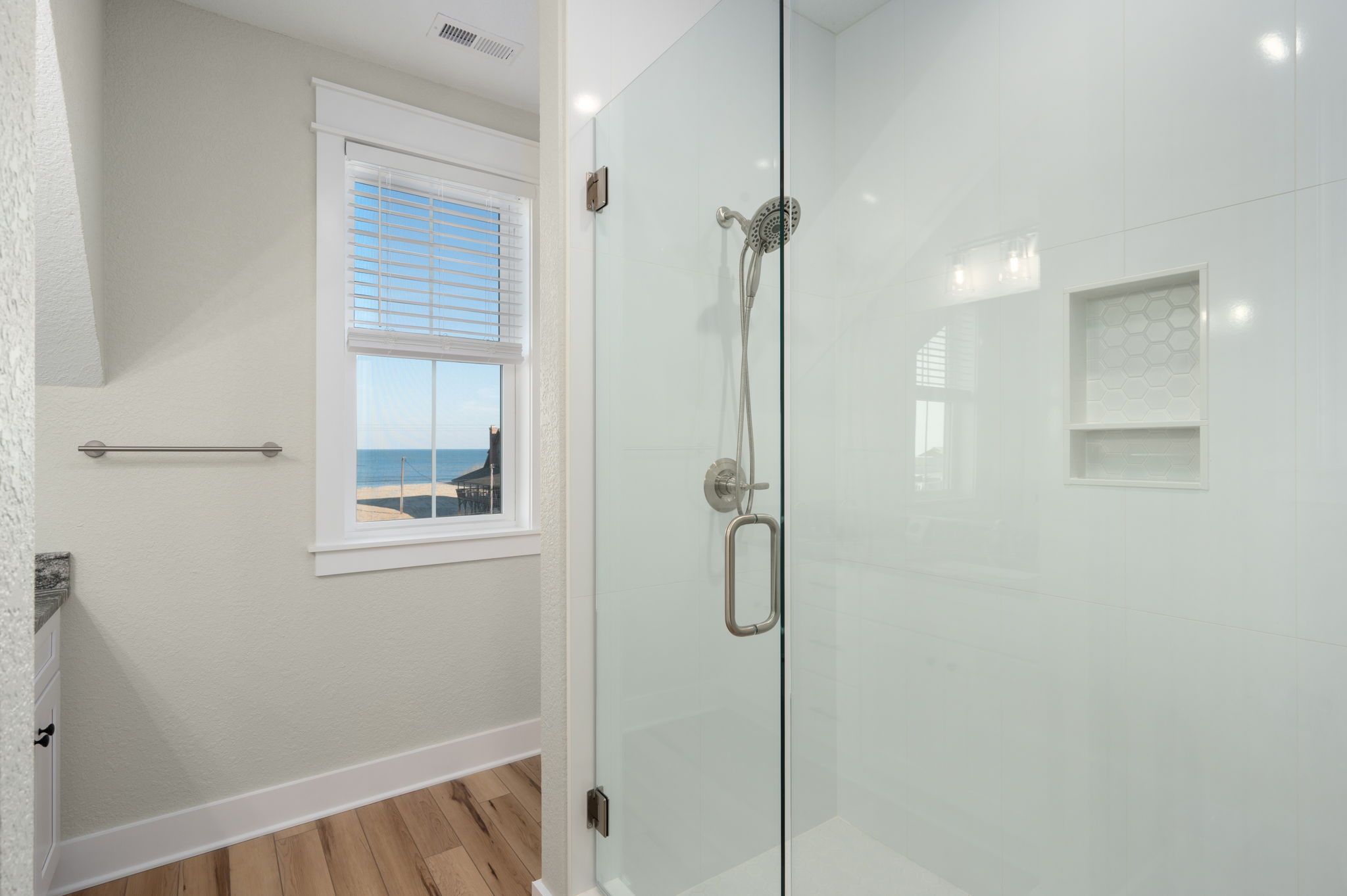 Ein modernes Badezimmer mit Duschkabine aus Glas, einem Fenster mit Jalousien und Meerblick.
