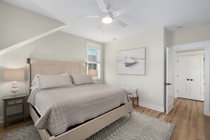 A bedroom with a bed, a nightstand, a ceiling fan, a window with blinds, a door, and a framed picture on the wall.