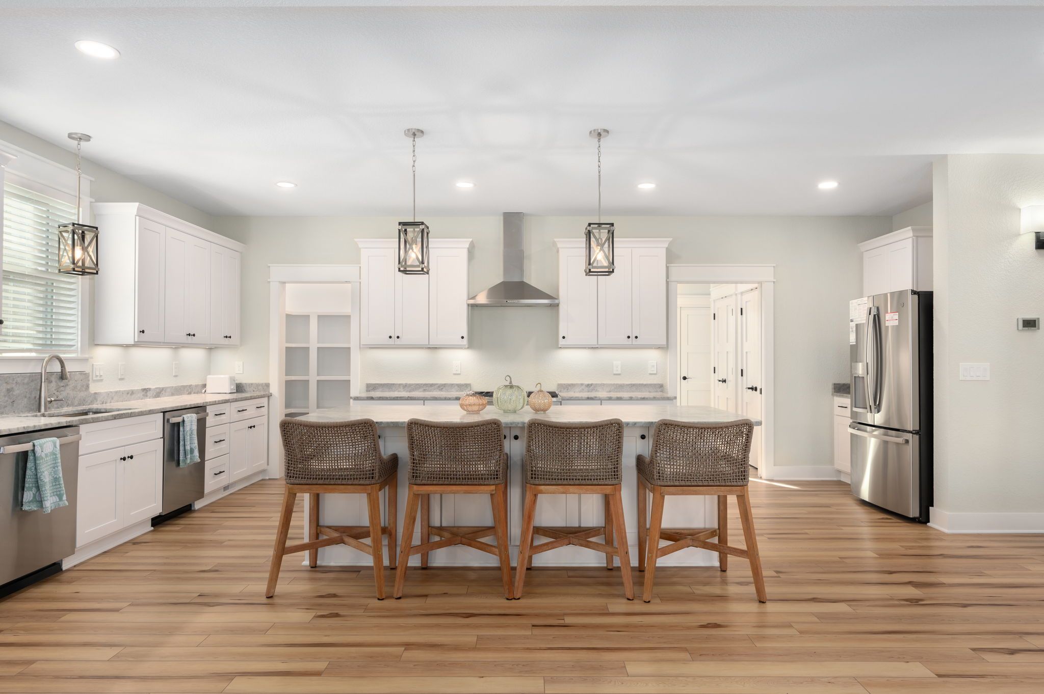 A modern kitchen with white cabinets, a central island with bar stools, and stainless steel appliances.