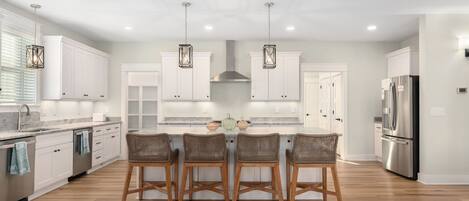 A modern kitchen with white cabinets, a central island with bar stools, and stainless steel appliances.