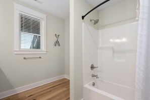 Un baño con ventana, ducha y suelo de madera.