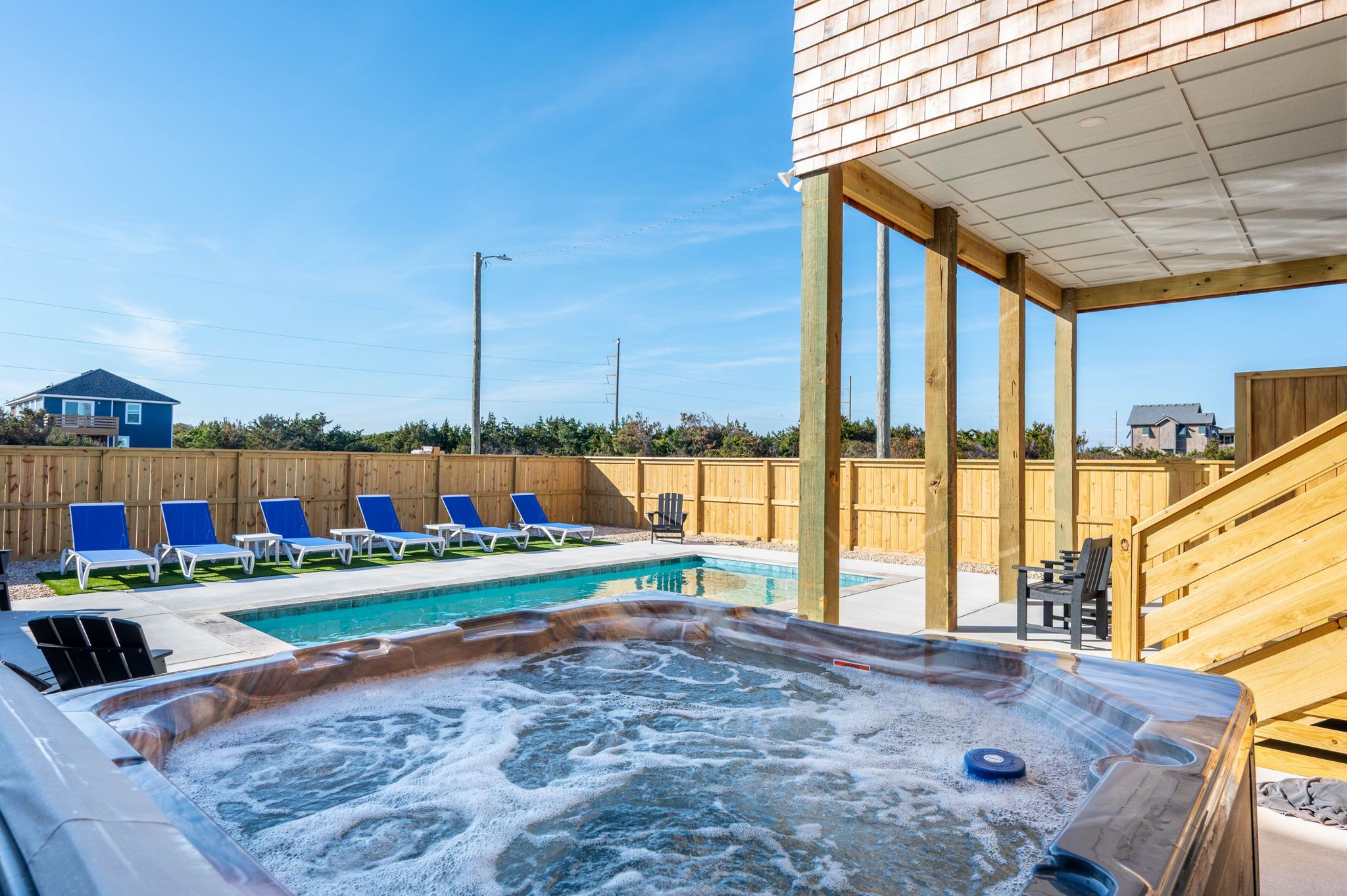 Uma banheira de hidromassagem com um deck de madeira e cadeiras de descanso, uma piscina e um cercado de madeira.