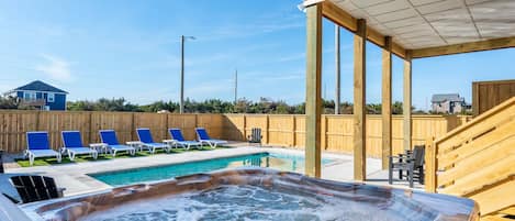 Uma banheira de hidromassagem com um deck de madeira e cadeiras de descanso, uma piscina e um cercado de madeira.