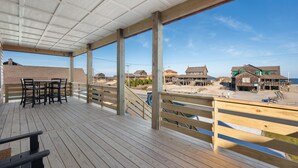 A wooden deck with a table and chairs, overlooking a beach with houses and a clear sky. - Nags Head 369: New Construction, Private Pool, Hot Tub, Ocean Views! (Nags Head)