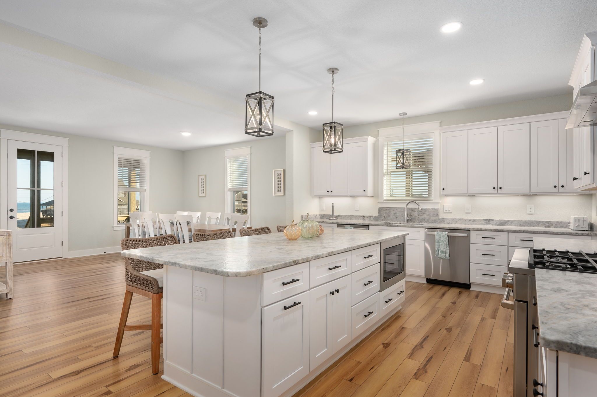 A spacious kitchen with white cabinetry, a large island, wooden flooring, and pendant lighting.