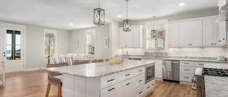 A spacious kitchen with white cabinetry, a large island, wooden flooring, and pendant lighting.