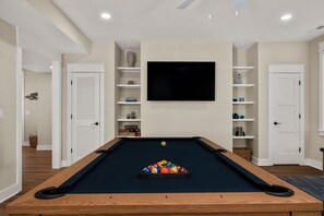 Une table de billard sur laquelle est fixée une télévision, le tout entouré de portes blanches et d’étagères contenant divers objets.
