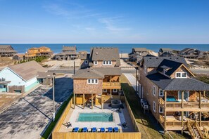 A beachfront property with a swimming pool, multiple decks, and a view of the ocean.