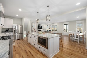 Una cocina amplia con electrodomésticos modernos, una isla grande y un comedor con sillas blancas.