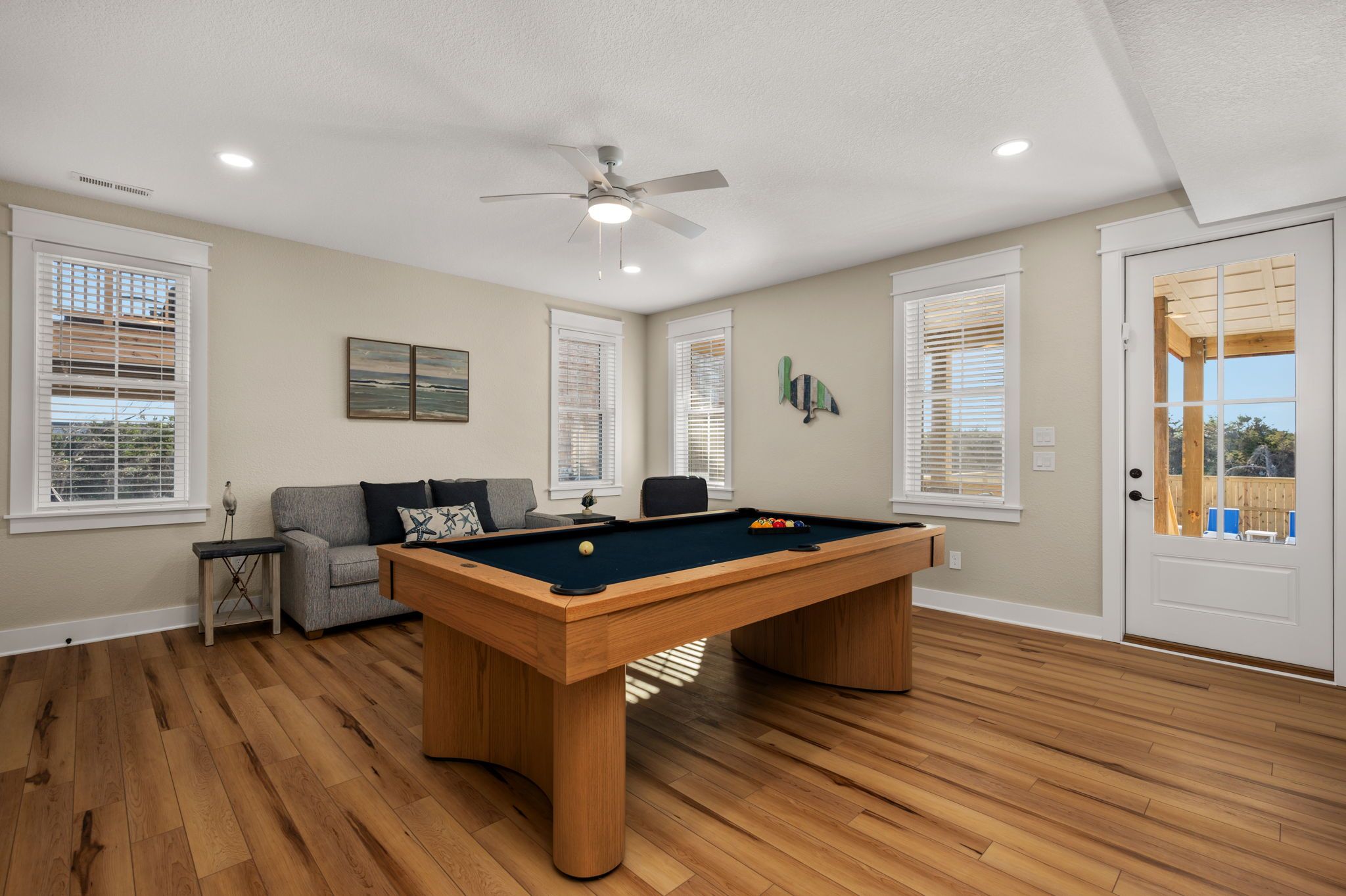 A room with a pool table, a ceiling fan, and a sofa.