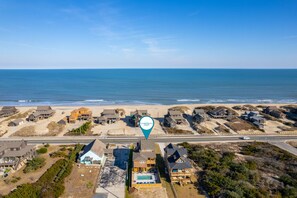 An aerial view of a coastal area with beach houses, a swimming pool, and a clear view of the ocean.