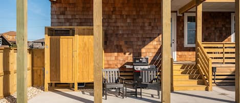 Eine überdachte Terrasse mit Grill, Holzstühlen und einer Holztreppe zu einer Tür.