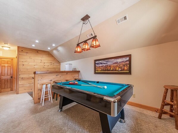 Una mesa de billar en una habitación con paredes de madera y un cuadro en la pared.