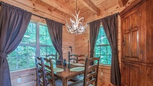 A wooden cabin interior with a dining table, chairs, a chandelier, and a cabinet.