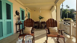 A covered patio area with wooden furniture, a table with drinks and seashells, and a view of palm trees. - Charming 2-bedroom ocean front condo in wonderful Las Terrenas (LasTerrenas)