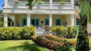A two-story building with a balcony on the upper floor, surrounded by lush greenery and flowering plants. - Charming 2-bedroom ocean front condo in wonderful Las Terrenas (LasTerrenas)