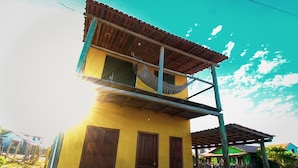 A two-story building with a yellow facade, a wooden balcony, and a hammock hanging from the upper floor. - Hospedaria Labelle - Xandó Caraíva (Porto Seguro)