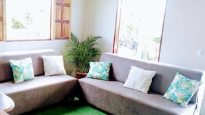 A living room with a grey sectional sofa, a wooden table, and a potted plant. - Hospedaria Labelle - Xandó Caraíva (Porto Seguro)