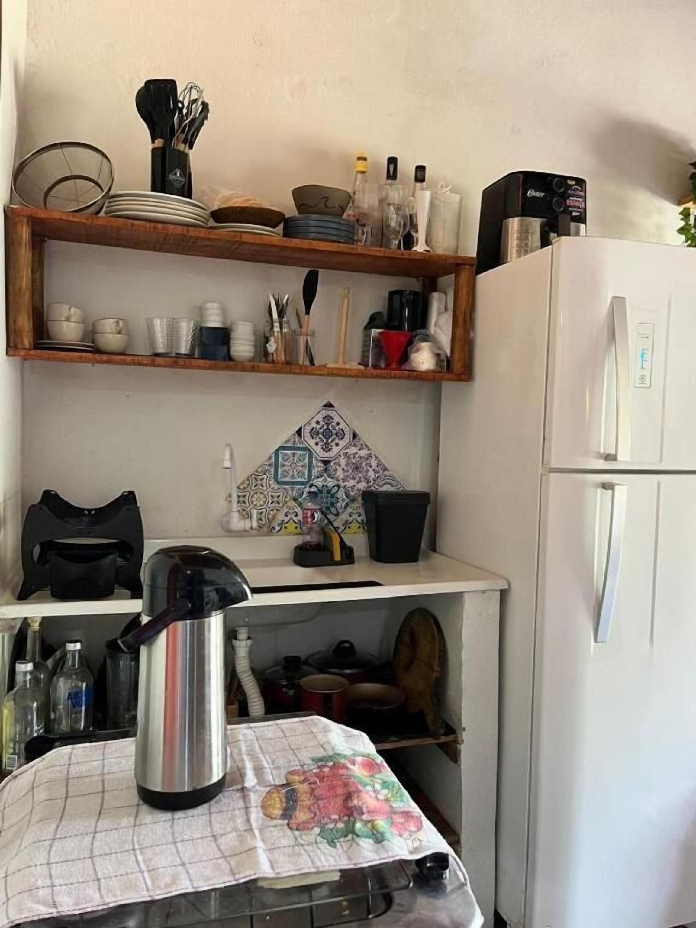 Cozinha com geladeira, prateleiras com louças, chaleira e painel de backsplash estampado.