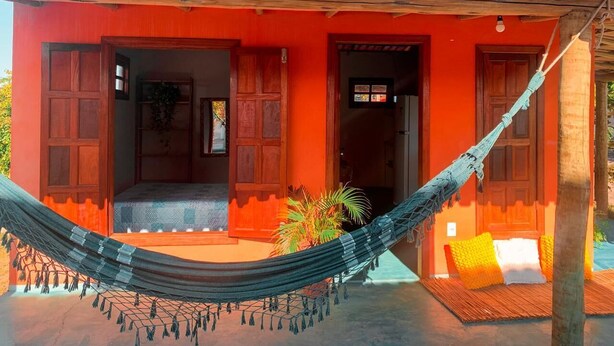 A red building with a tiled roof, a hammock, and a small porch area. - Hospedaria Labelle - Xandó Caraíva (Porto Seguro)