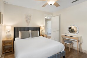 Un dormitorio con cama, mesitas de noche, tocador con espejo y ventilador de techo.
