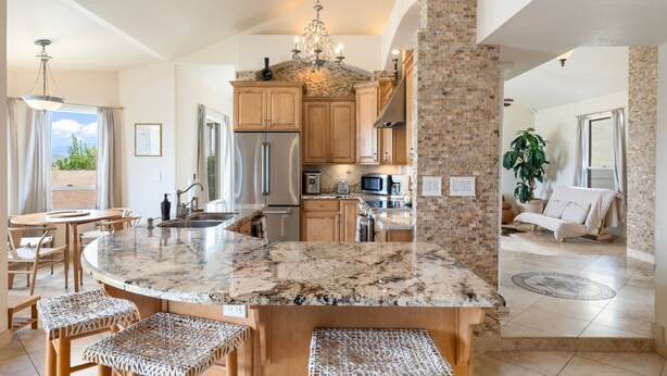 A spacious kitchen with granite countertops, wooden cabinets, and a central island with bar stools. - Heated Pool, Waterslide, Mountain Views 3 Bedroom 2 Bathroom Tuscan Home (Fountain Hills)