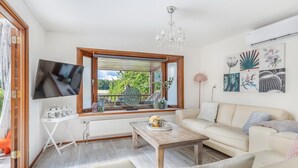 Una sala de estar con televisión, una mesa de madera, un sofá y un ventanal con vistas a la vegetación.