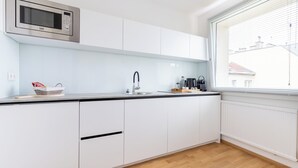 Een moderne keuken met witte kasten, een roestvrijstalen magnetron, een spoelbak en een raam met zonwering.