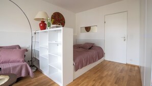 Een slaapkamer met een bed, een witte kledingkast, een lamp en een spiegel.