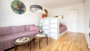 Een moderne woonkamer met een bank, twee bijzettafels, een lamp en een kleurrijk abstract schilderij.