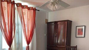 Ein Schlafzimmer mit Bett, Kleiderschrank, Schreibtisch und Deckenventilator.