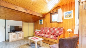 Ett mysigt rum med ett träpanelat tak, en soffa med mönstrade kuddar, en tv, ett litet bord och en stol.