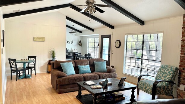 A spacious living room with a brown leather sofa, teal cushions, a wooden coffee table, and a dining area with a small table and chairs.