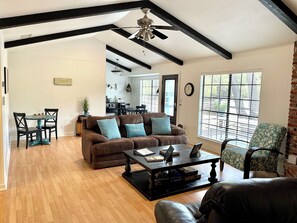 A spacious living room with a brown leather sofa, teal cushions, a wooden coffee table, and a dining area with a small table and chairs. - NEW! Private Wooded Escape Between 2 Lakes • Walk to 1 • BYO Boat • Pet-friendly (Austin)