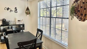 A dining area with a table and chairs, a coffee station, and a window with blinds.