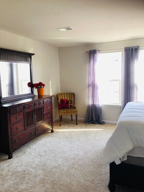 Une chambre à coucher avec un lit, une commode, une chaise et une fenêtre avec des rideaux.