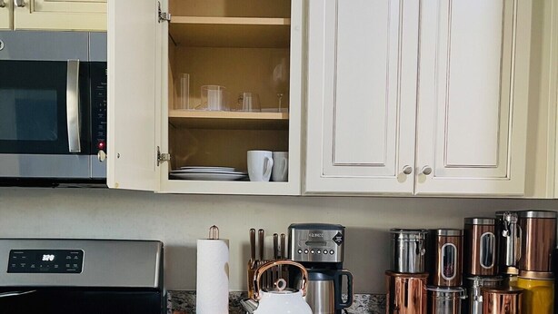 Een keuken met witte kasten, een roestvrijstalen oven, een koffiezetapparaat en koperen kookgerei.