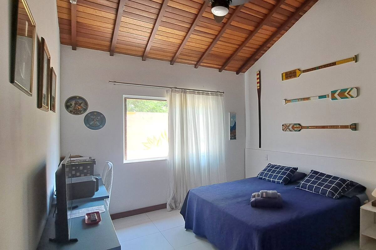 A bedroom with a bed, a desk, a chair, a window with curtains, and wall decorations including a painting and wall-mounted items.