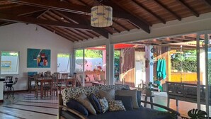 A spacious living area with a sofa, dining table, and chairs, a kitchen area, and large windows offering a view of the outdoors. - Casa Santa María Búzios (Búzios)